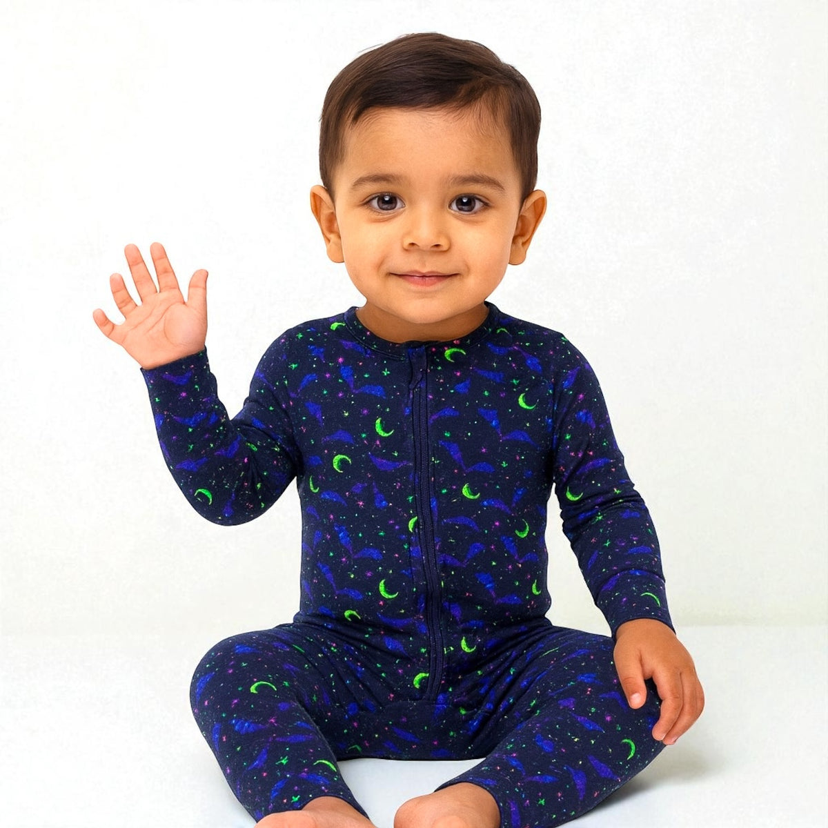 Child waving while wearing Cosmic Bats Bamboo Zipper Sleeper featuring a cosmic pattern with bats, stars, and moons.