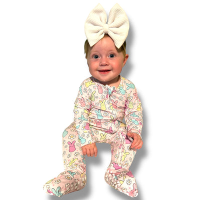 Baby wearing a colorful Easter Bunny zipper sleeper with a big white bow headband, smiling cheerfully.