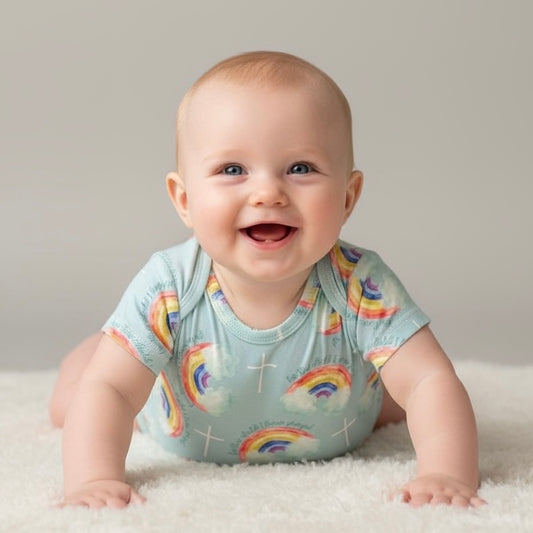 Baby wearing a light blue onesie with rainbow patterns on a neutral background