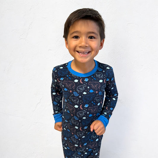 Happy boy wearing Constellation Bear long sleeve two-piece pajamas with colorful animal and star patterns.