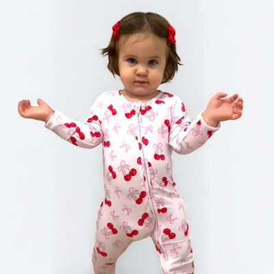 Toddler girl in Cherry Coquette bamboo zipper sleeper with cherry print, smiling and posing playfully.