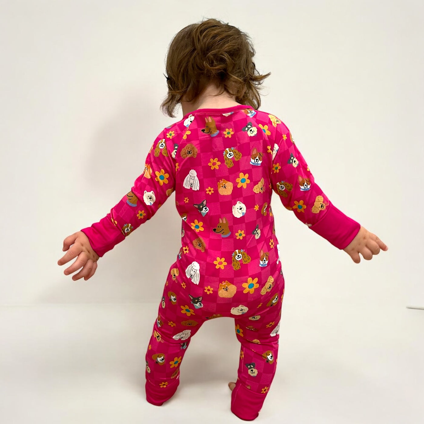 Child in pink floral pajamas featuring a colorful design, showcasing the back view of the outfit.