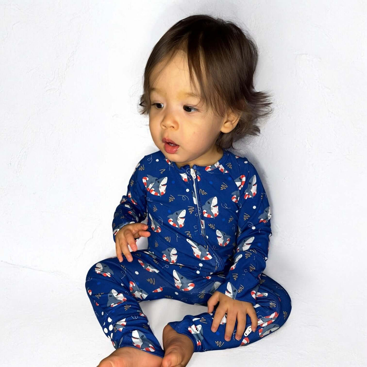 Baby wearing Shark Floaties blue bamboo zipper sleeper, sitting against a white background.