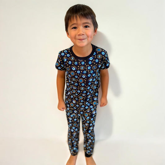 Child wearing Evil Eye black short sleeve two-piece pajamas, featuring colorful eye patterns, smiling against a plain background.