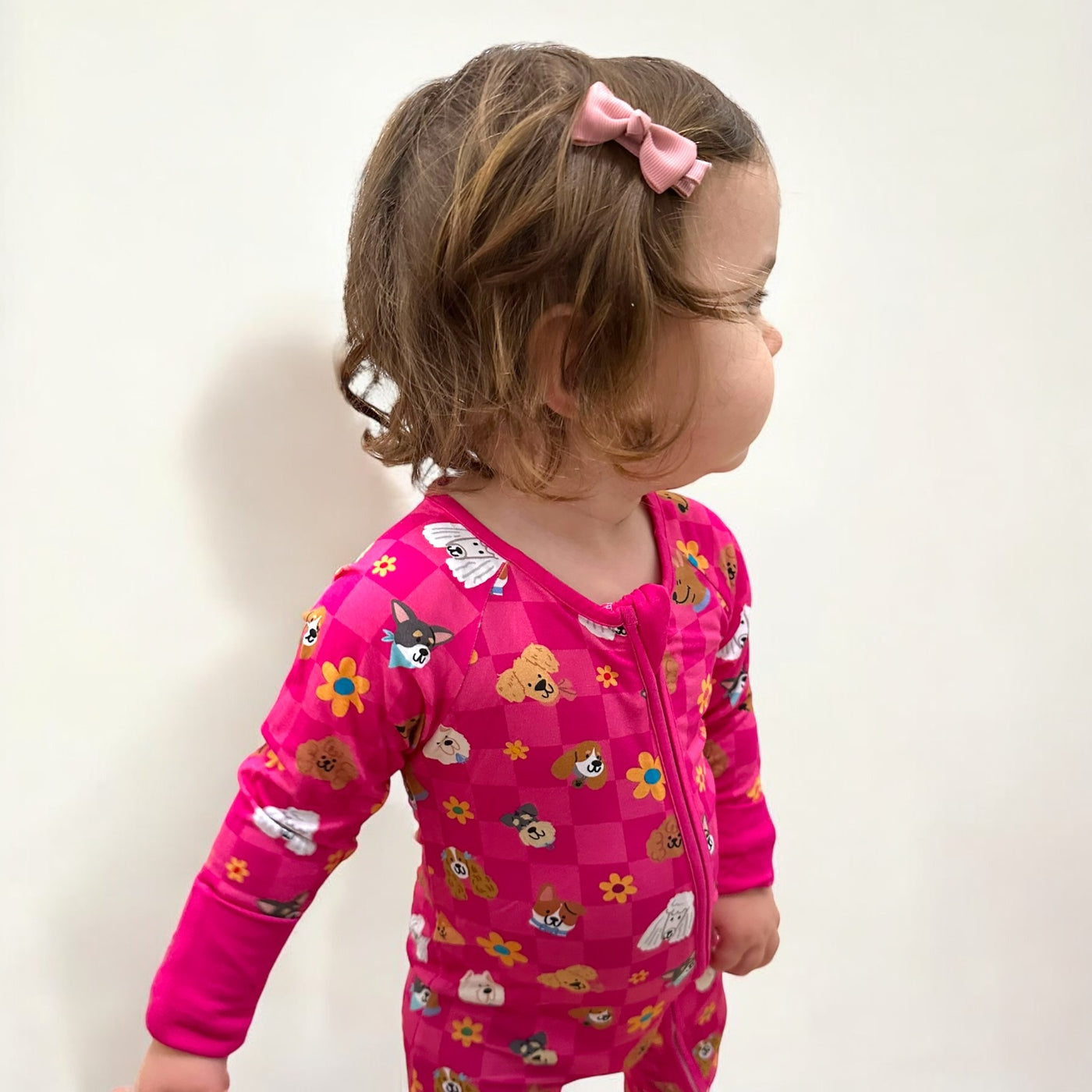 Toddler wearing a pink Checkered Pups bamboo zipper sleeper with playful dog prints and flowers.
