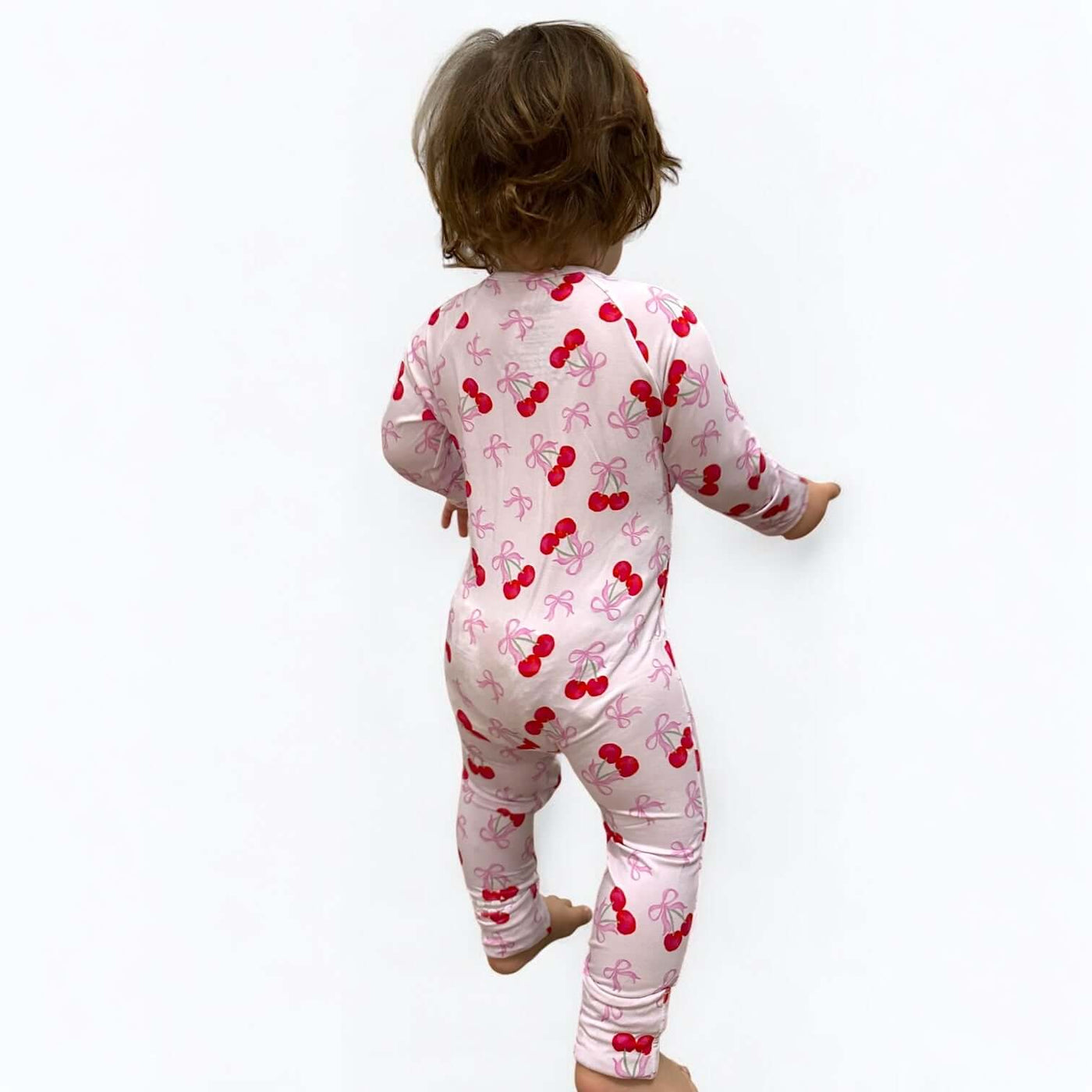 Toddler wearing a Cherry Coquette bamboo zipper sleeper with a pink cherry pattern.