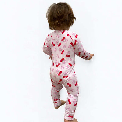 Toddler wearing a Cherry Coquette bamboo zipper sleeper with a pink cherry pattern.